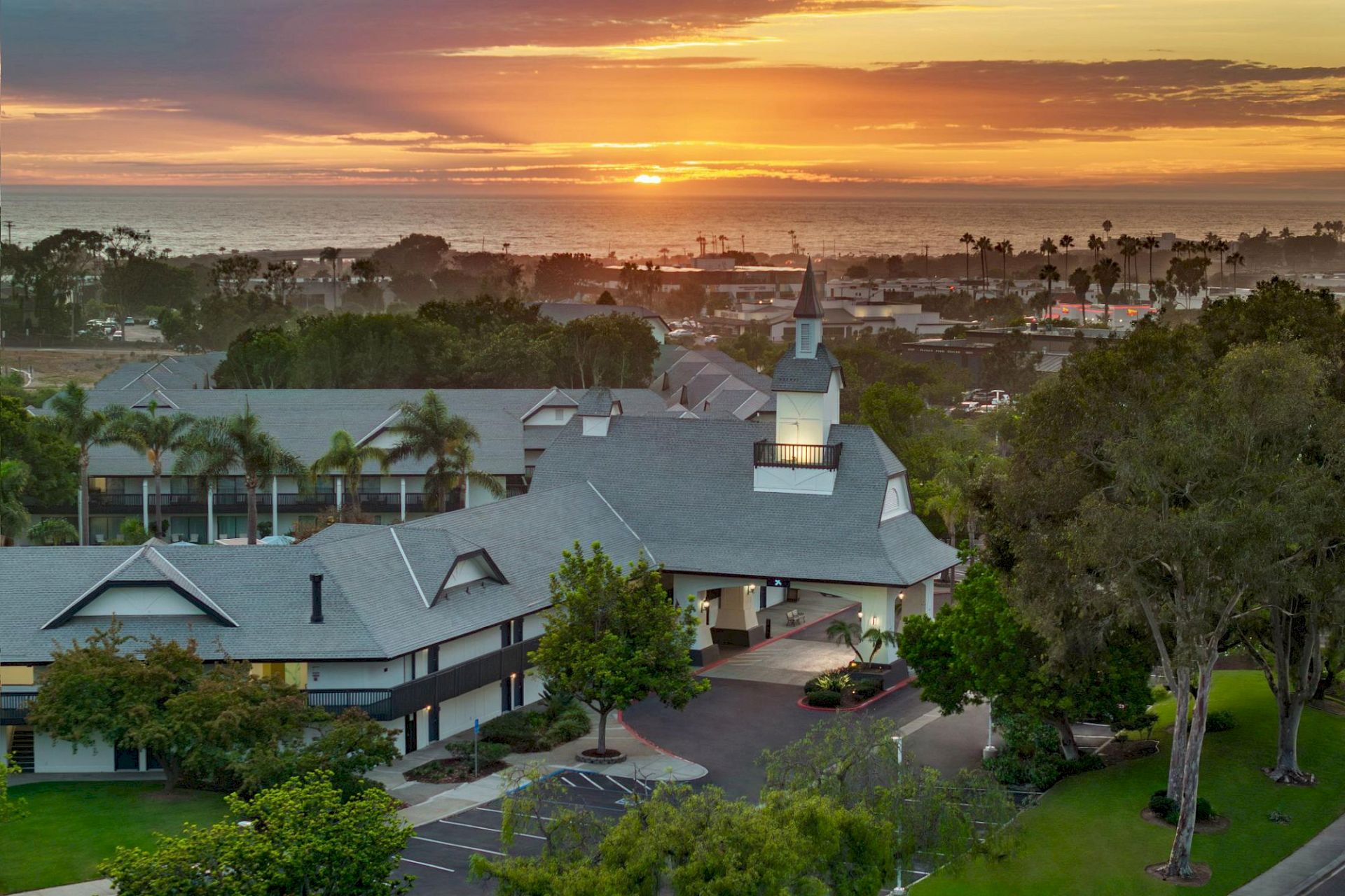 A coastal resort at sunset, with palm trees, white buildings, and the ocean glowing under a golden sky.