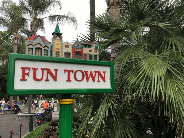 A park sign reading &ldquo;FUN TOWN&rdquo; sits by a colorful toy-like building and tall palm trees.