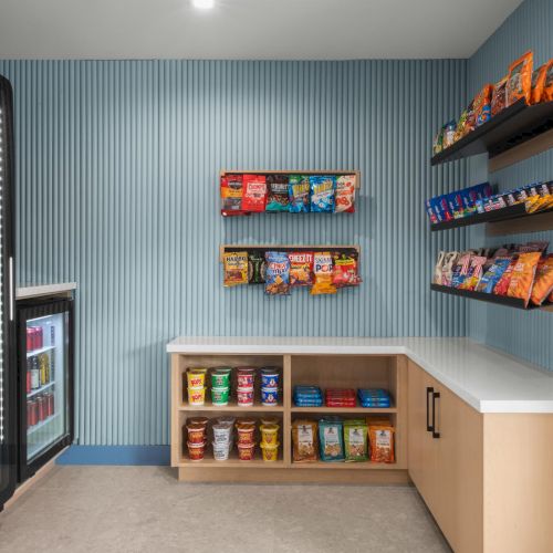 A convenience store snack display with a lit drink fridge and shelves stocked with candy, chips, and soda.