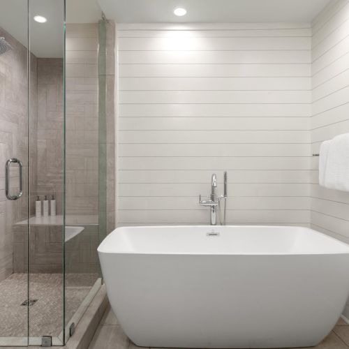 A modern bathroom with a glass shower, rain showerhead, tiled walls, a freestanding bathtub, and a folded white towel on a rail.