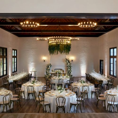 A candlelit wedding banquet hall with chandeliers, set tables, and a floral arch over the central serving area.